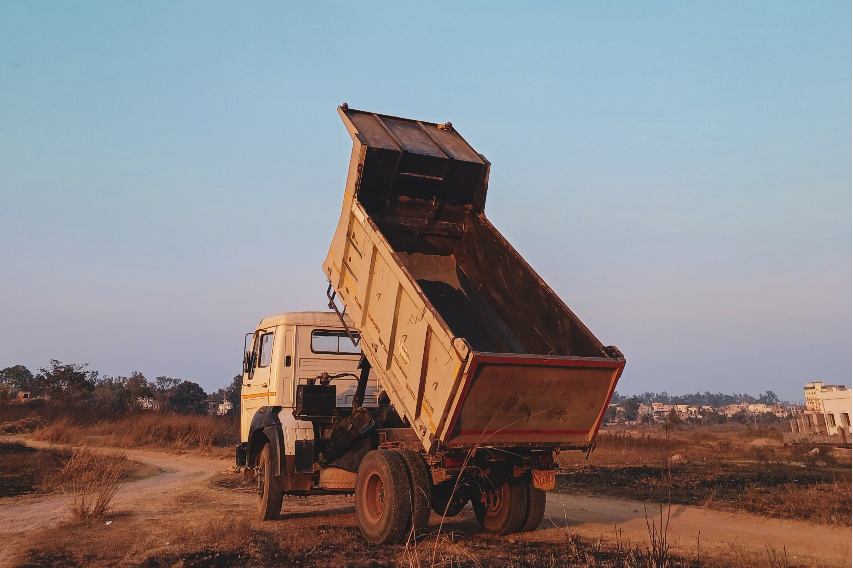 A yellow dump truck stands on a dirt track with its dump bed upright