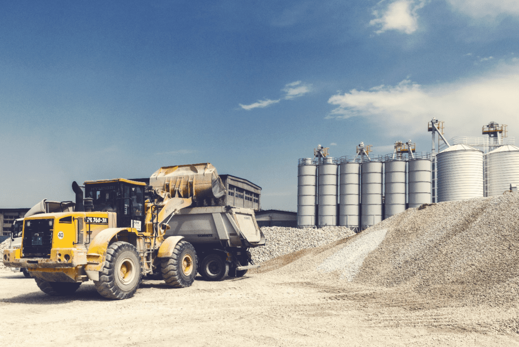 A power loader and dump truck pictured with gravel in front of a factory