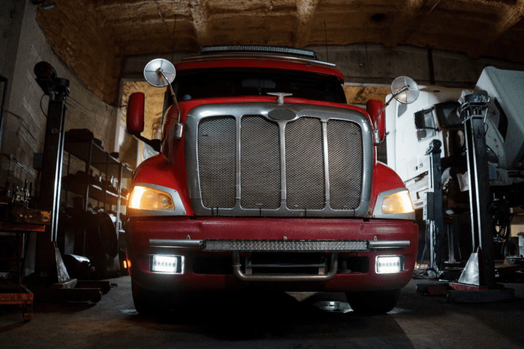 A red trailer truck stands in a repair workshop with lights on