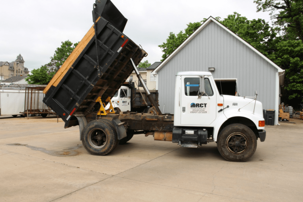 Dump truck with static upright bed secured by BedLock truck bed locks for safe maintenance in front of a workshop.