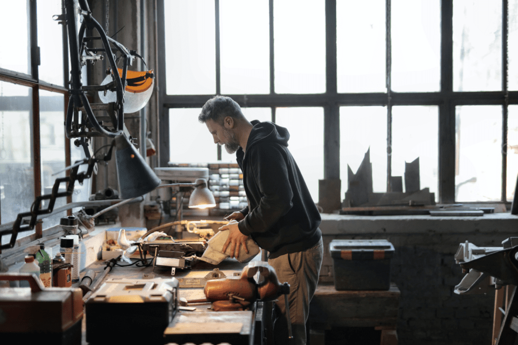 A man working with metal tools near a large window in a workshop