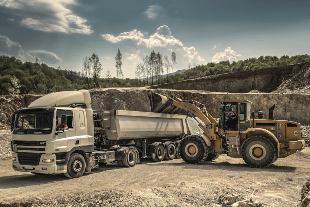 A yellow loader loading a white dump truck at a quarry site.