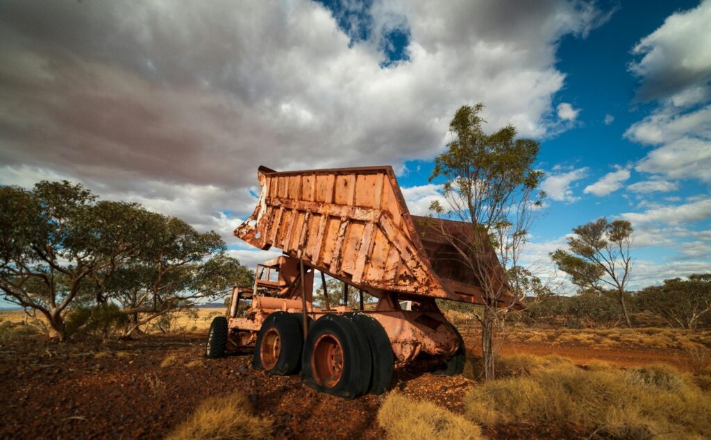 A rusty dump truck lifts its dump bed at a construction site amidst trees and sparse foliage, highlighting how powerful these machines are and shedding light on the potential safety hazards in truck repair