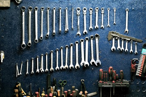 A variety of spanners hang on a textured blue wall with screwdrivers, allenkeys, and other tools visible at the bottom, highlighting how organization of tools can help with optimizing workflow in truck repair.