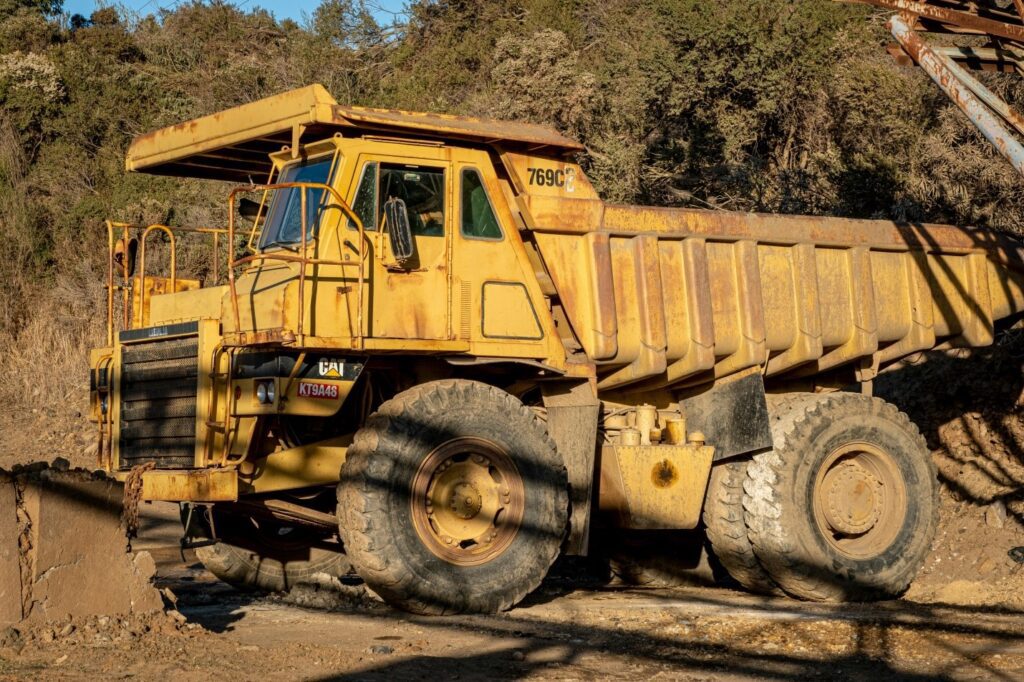 A large yellow Caterpillar dump truck on land with dense foliage in the background showcasing why truck repair safety regulations are so important.