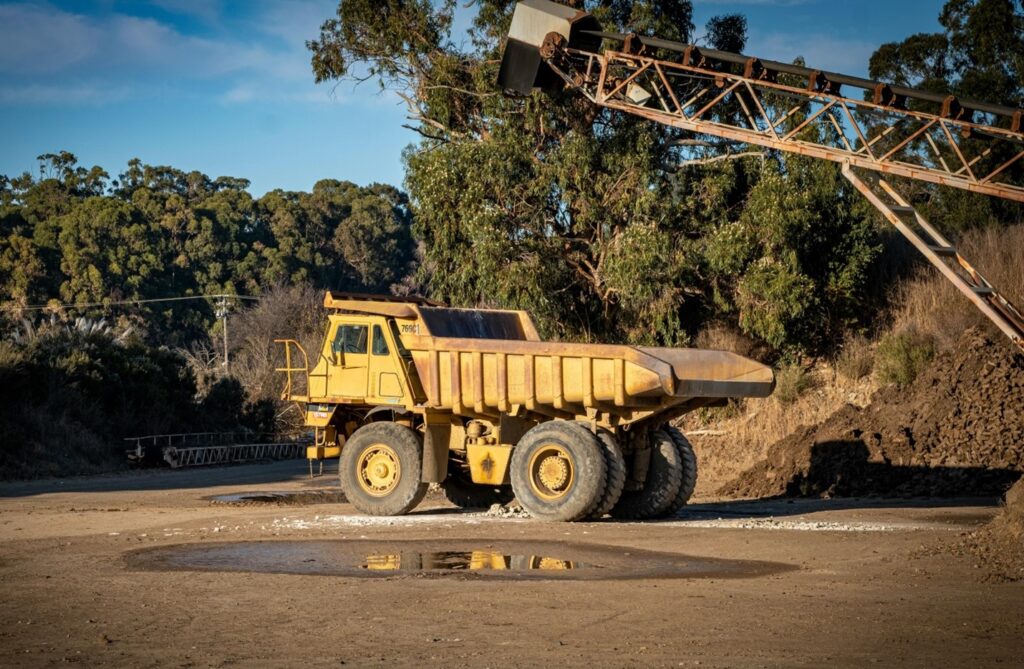 A large yellow dump truck stands at a construction site beside a puddle, showing that such heavy machinery warrants the need for stringent compliance in truck repair