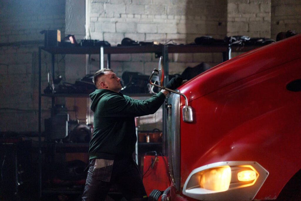 A technician wearing a green hoodie inspecting the front of a red dump truck.