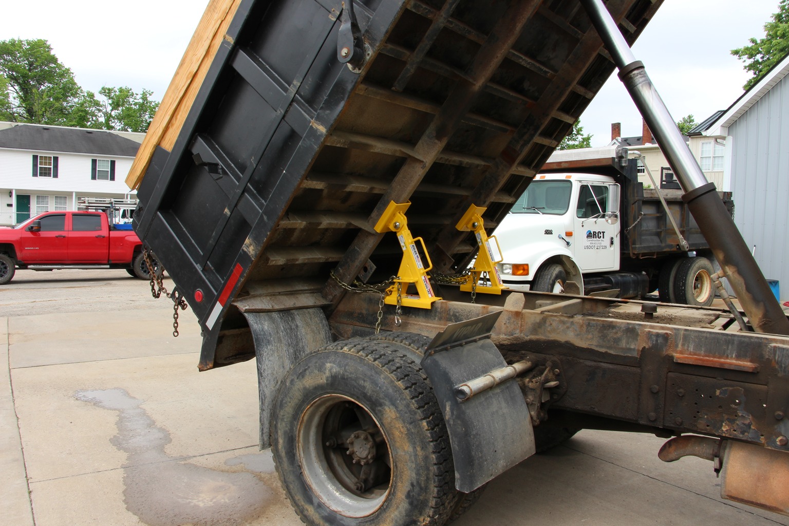 A close-up of a sturdy, yellow truck bed lock securing a raised dump truck bed.