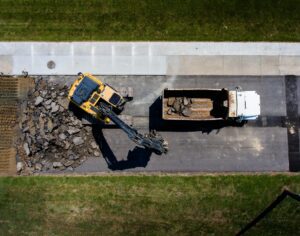 Aerial view of a white dump truck and yellow heavy equipment at a worksite during the daytime.