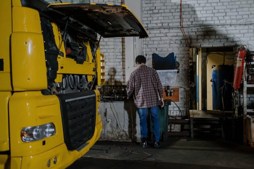 Mechanic inspecting and repairing a truck engine in a professional repair facility, focusing on safe maintenance practices.