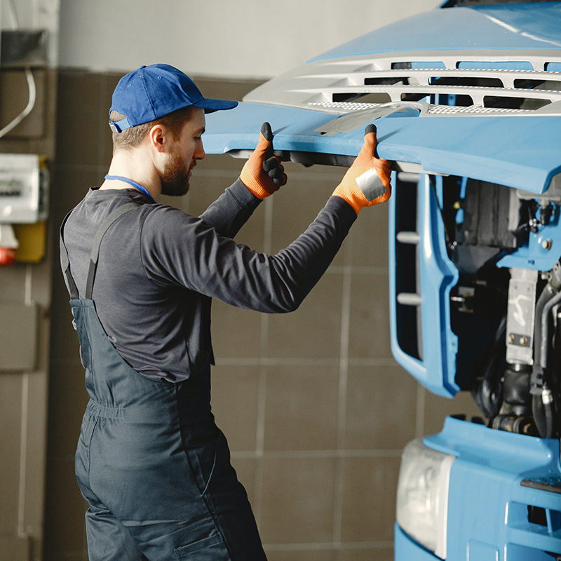Technician performing maintenance under a raised dump truck using proper safety procedures