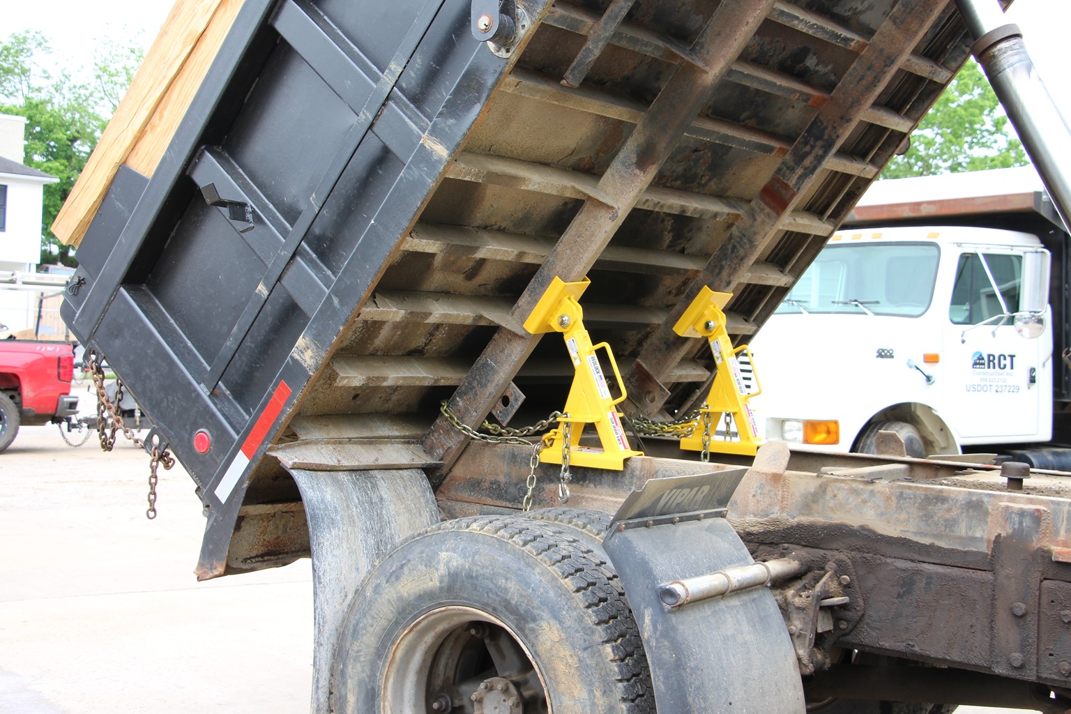 Two yellow BedLock safety stands installed beneath a raised dump truck bed with the truck cab visible in the background