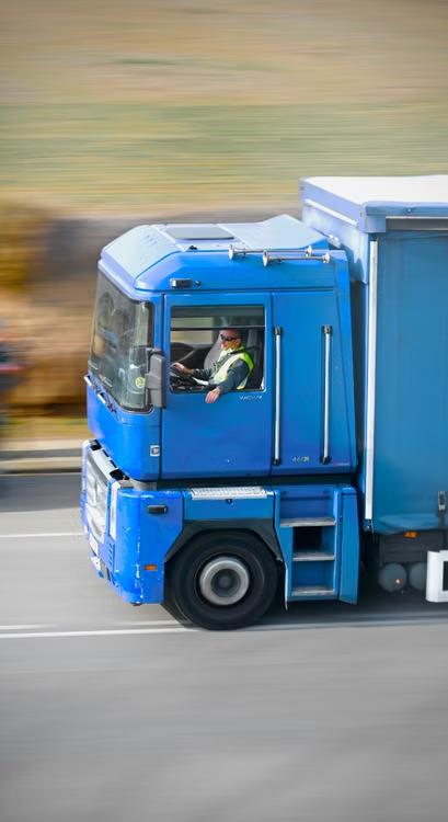 Blue truck with a box trailer driving down a highway with a motion-blurred background