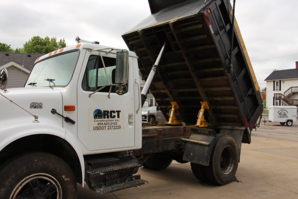White dump truck with its bed raised for maintenance in a driveway