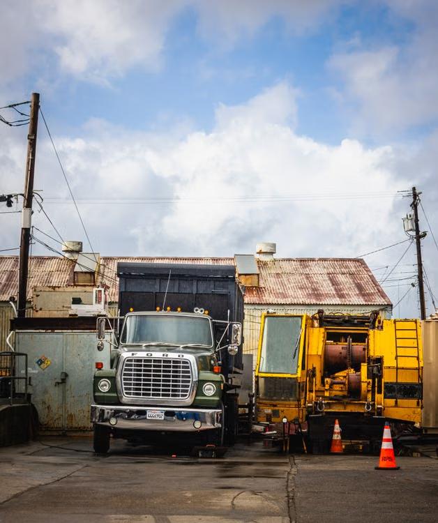 Older Ford dump truck parked next to industrial equipment in a work yard