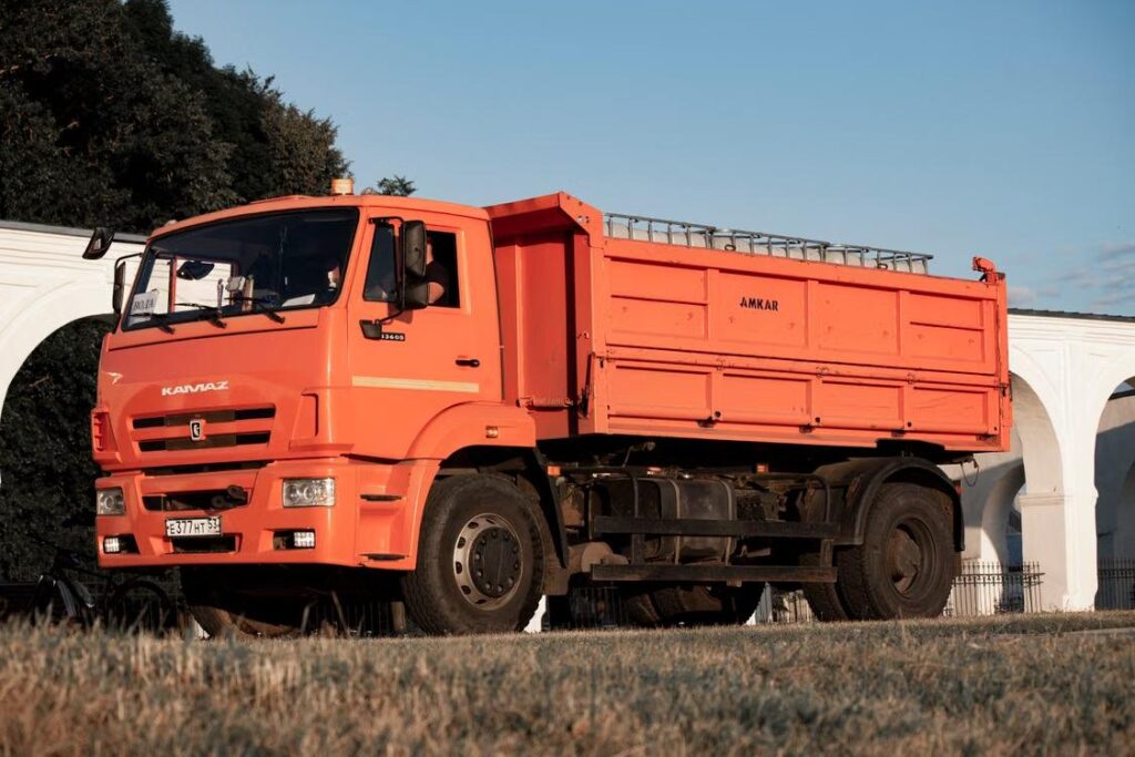 Orange dump truck with tipper bed parked near a decorative white archway
