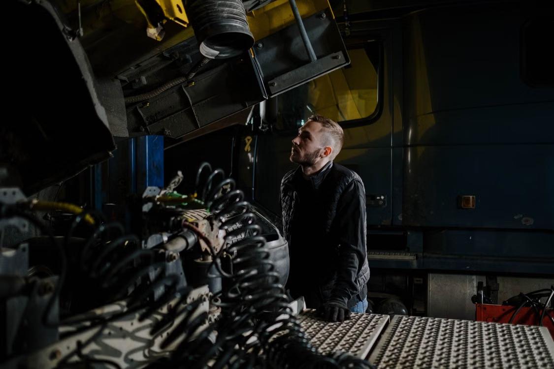 Technician inspecting an open engine compartment on a truck in a repair garage