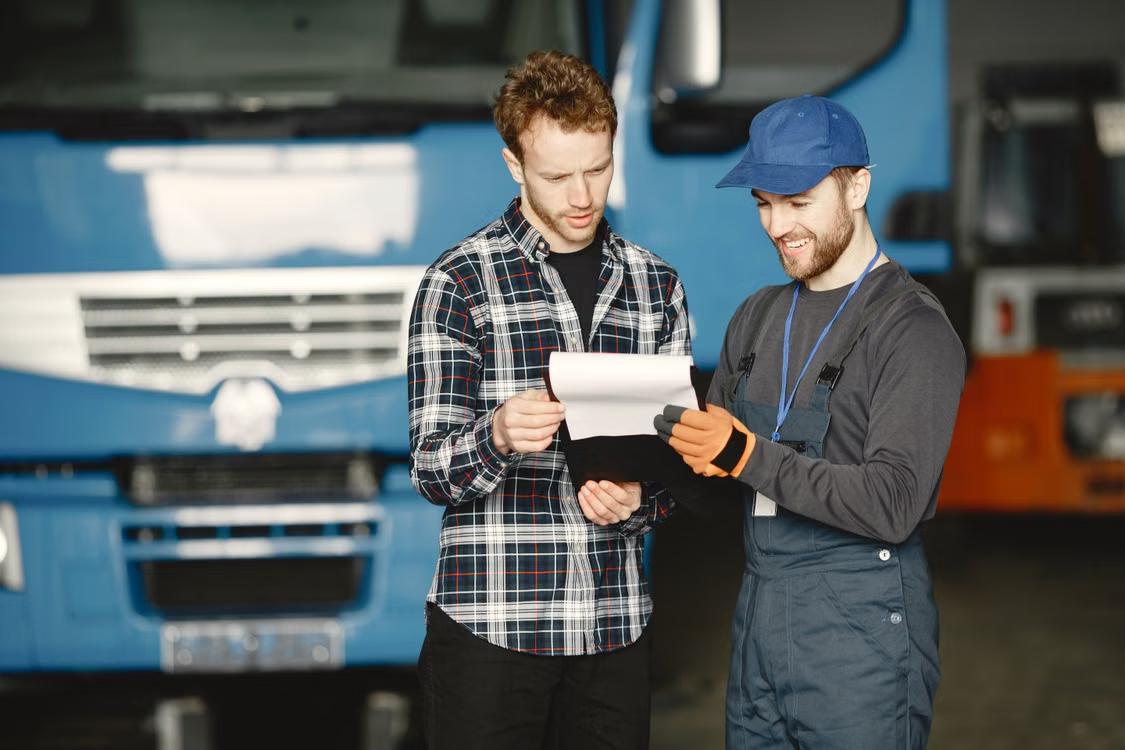 Two technicians reviewing paperwork on a clipboard in front of a truck in a repair shop