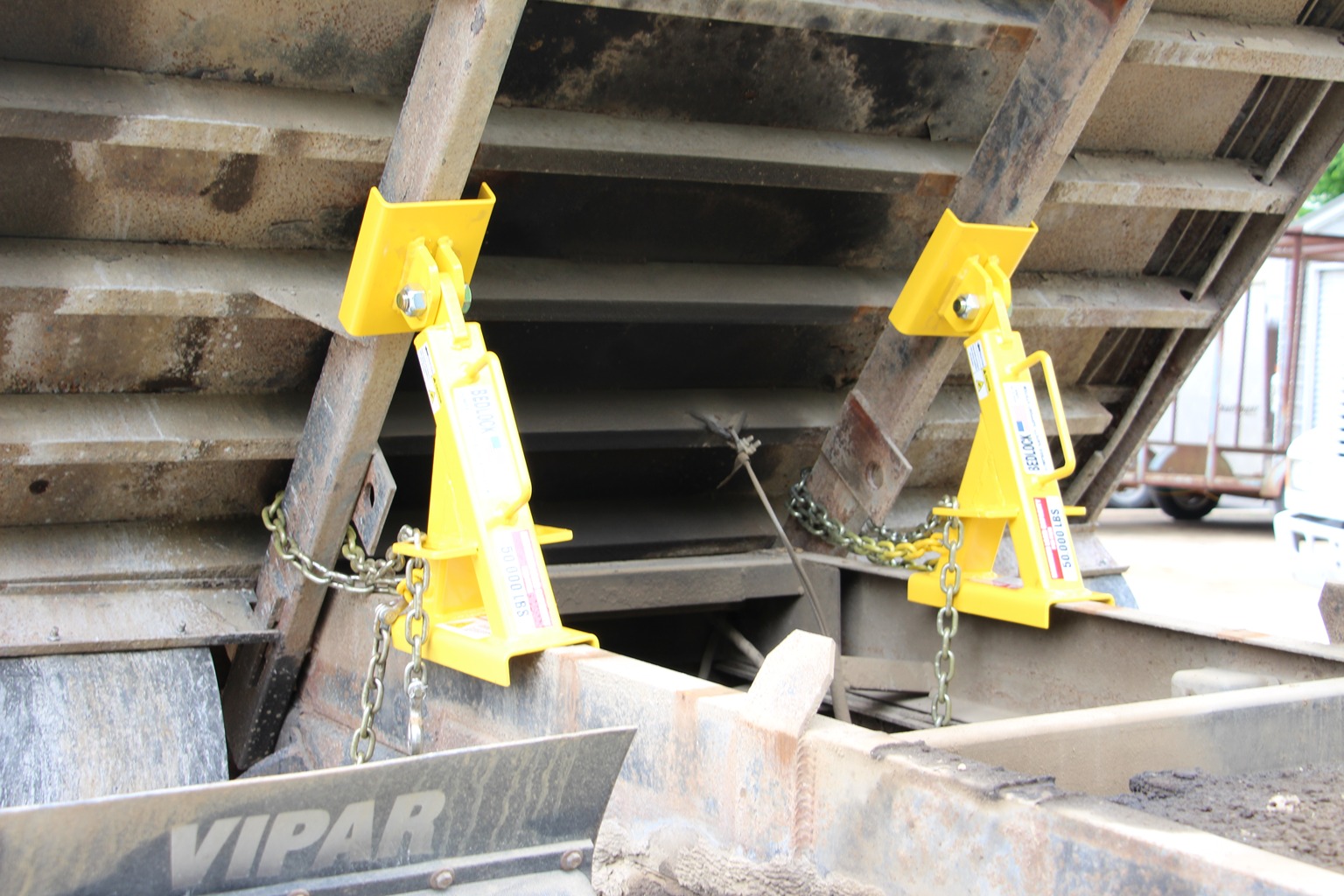 A technician working confidently beneath a dump truck bed secured by a mechanical support system.
